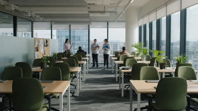 Open-plan office with rows of desks, green chairs and large windows